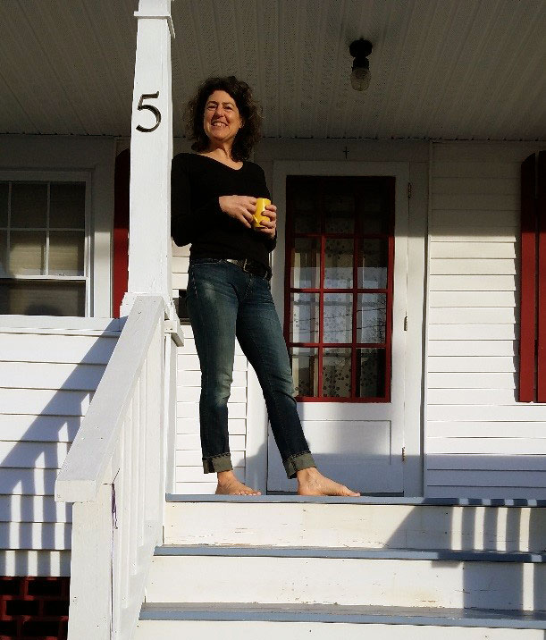 Clay standing on her front porch with a yellow coffee cup smiling. 