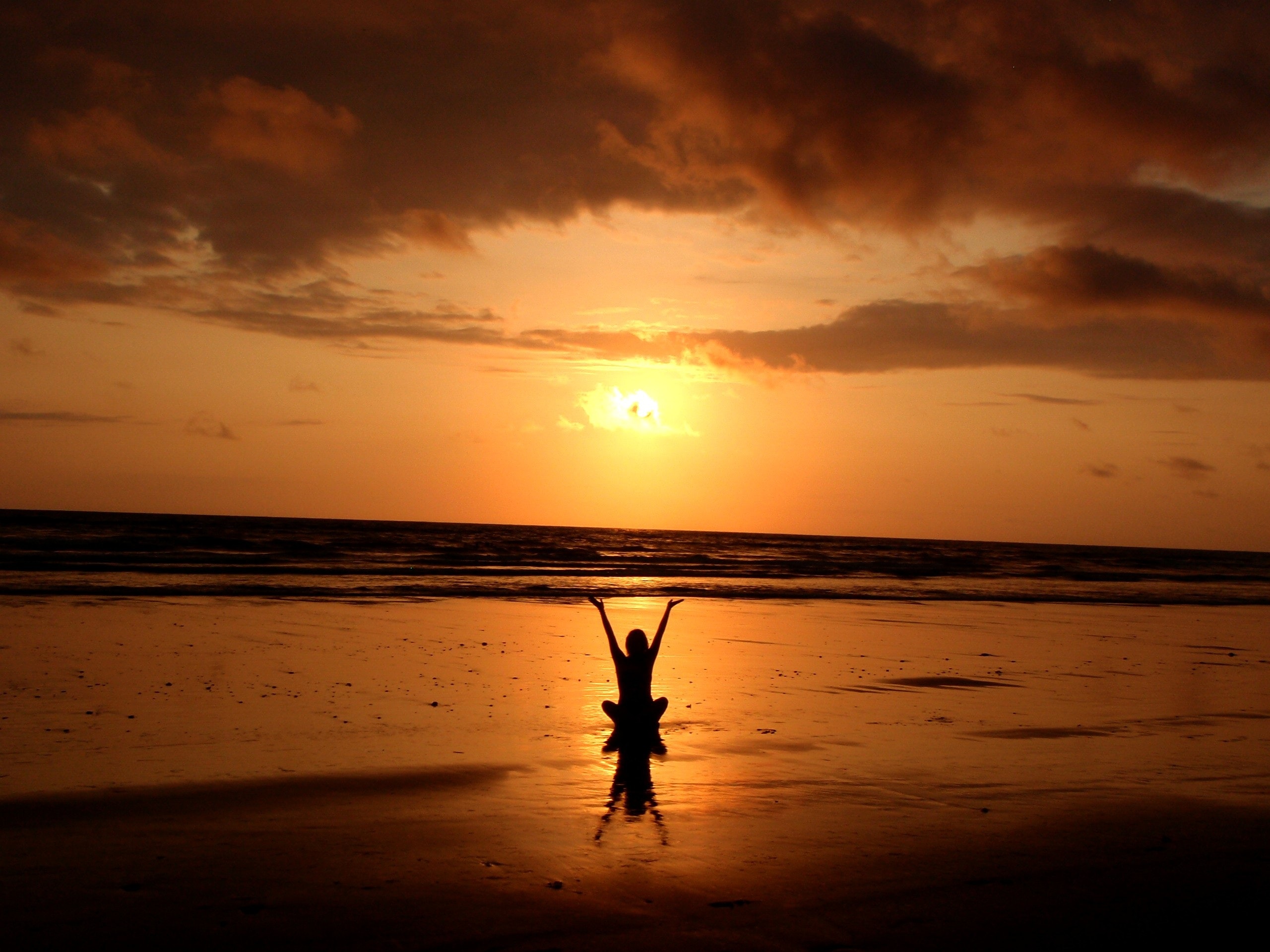 Person sitting on beach while the sun rises 