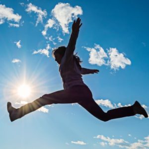 Photo of woman leaping in the air with blue sky in the background.