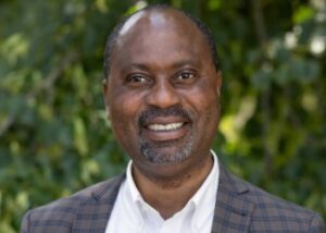 Banjo is an African-American man with mustache wearing a white collared shirt and gray suitcoat