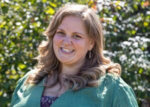 Bethany has light brown hair and a big smile; she is wearing an aqua green shirt