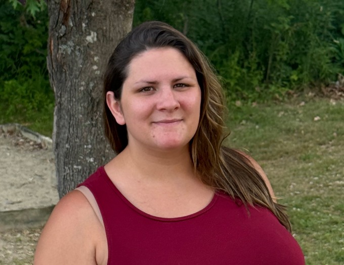 Briana Murico-1 (1) Briana is wearing a maroon tank top and is standing outside next to a tree