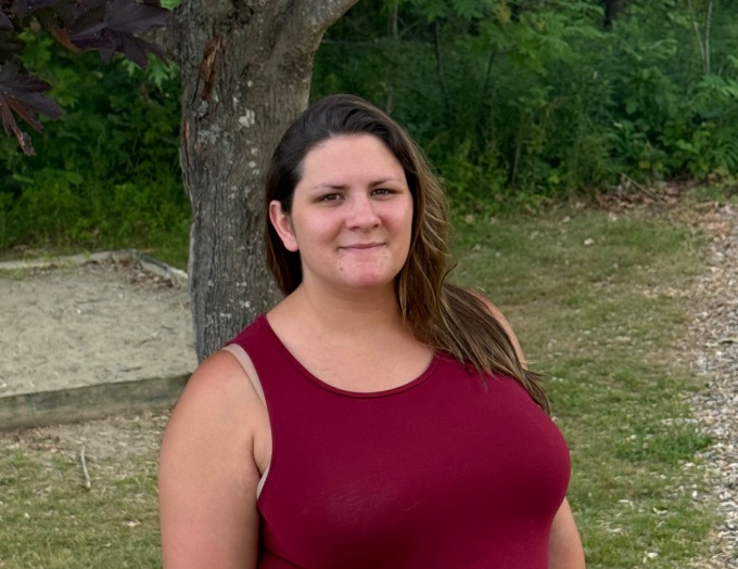Briana Murico stands outside in front of a tree wearing a maroon shirt