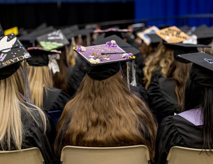 grads with colorful mortar boards in the foreground seen from the back